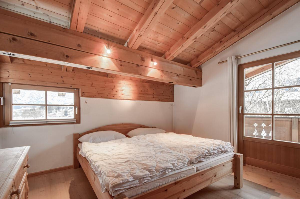 Helles Schlafzimmer mit Holzbalkendecke, Parkettboden und Zugang zu einem französischen Balkon.