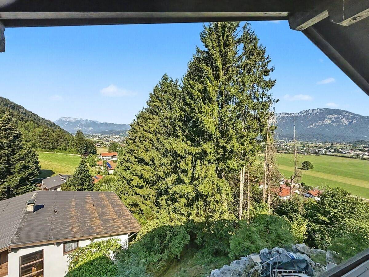Weitläufiger Blick über ein grünes Tal mit Bäumen und Bergen im Hintergrund.