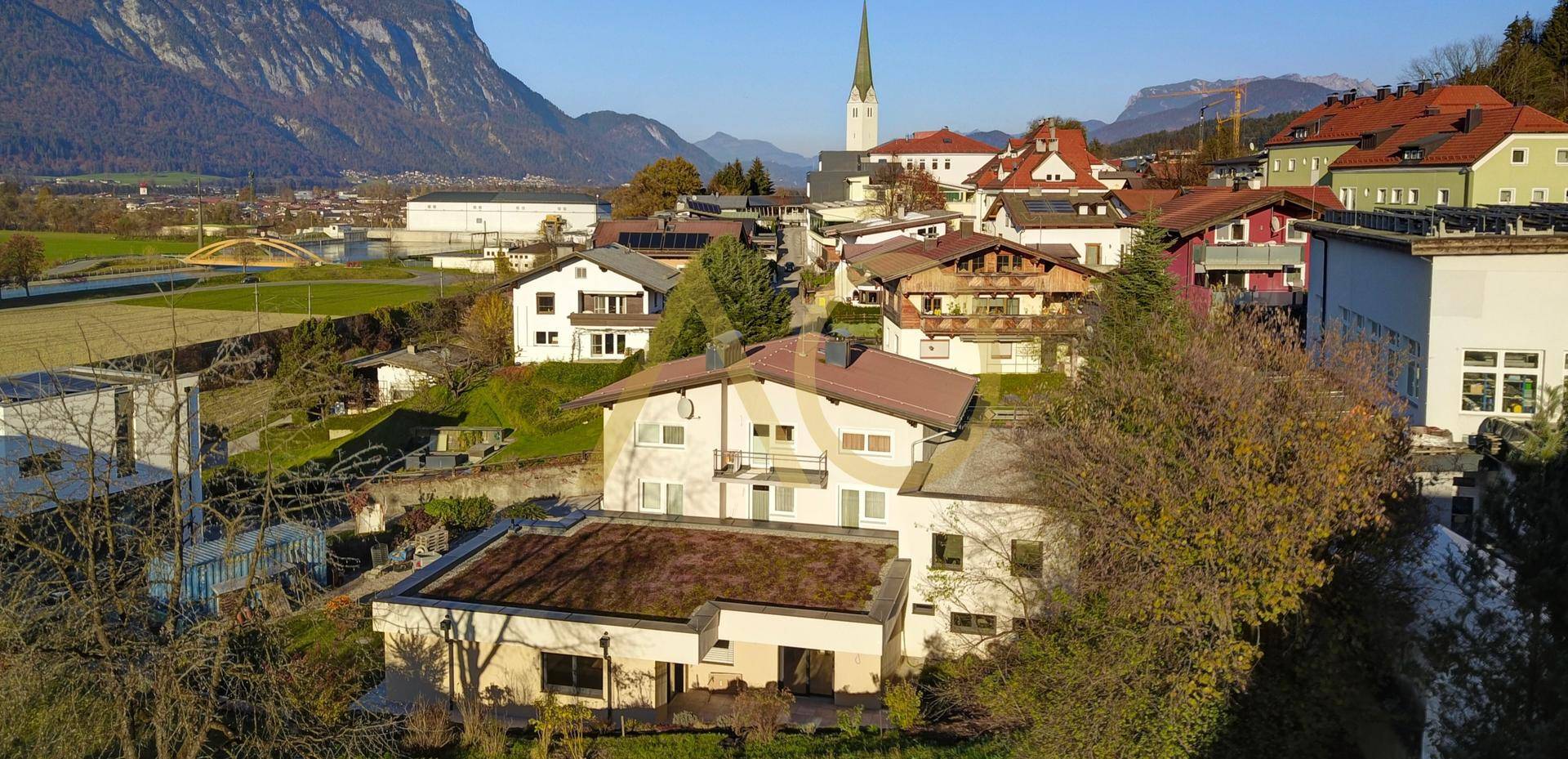 Panoramablick auf das Anwesen in ländlicher Umgebung mit Dorfkirche und majestätischen Bergen.