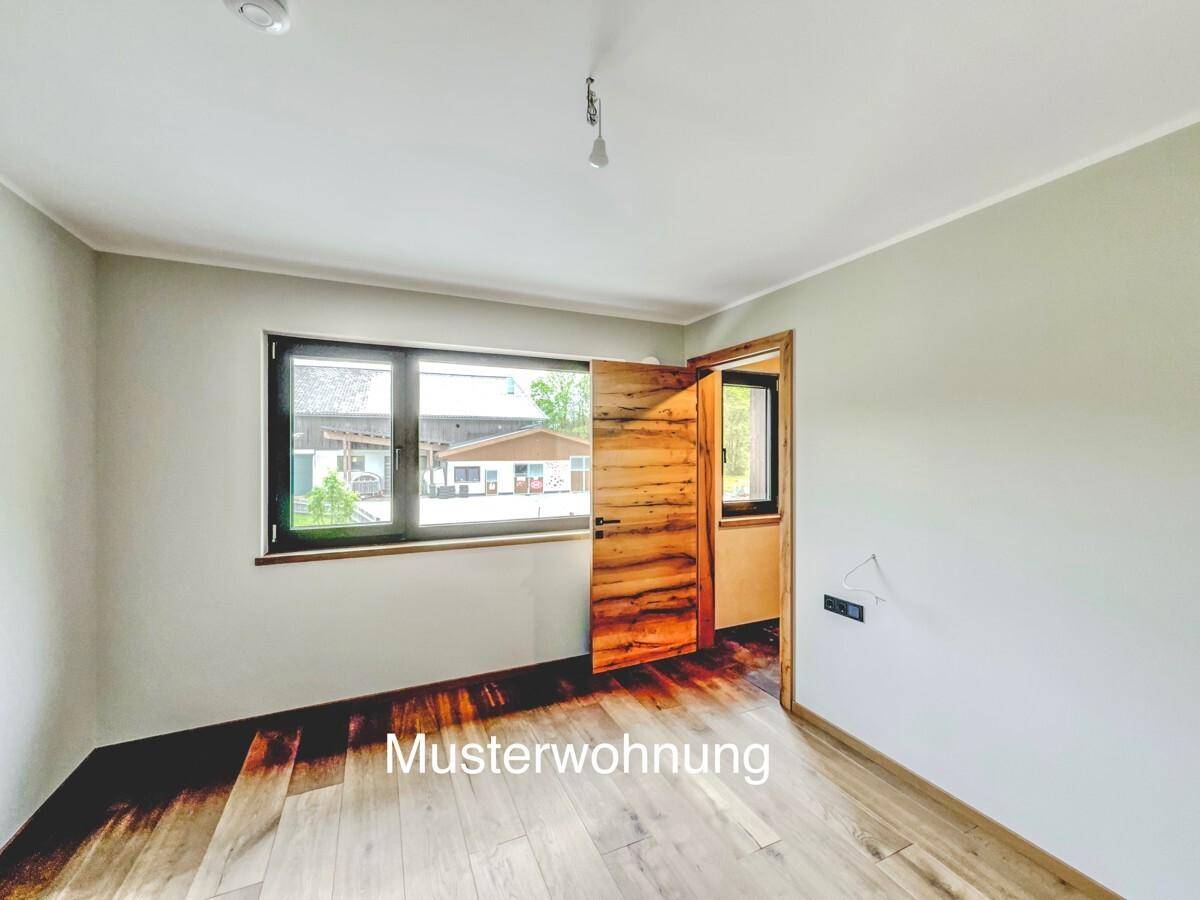 Helles Schlafzimmer einer Musterwohnung mit Holzboden und einem Fenster mit Blick ins Grüne.