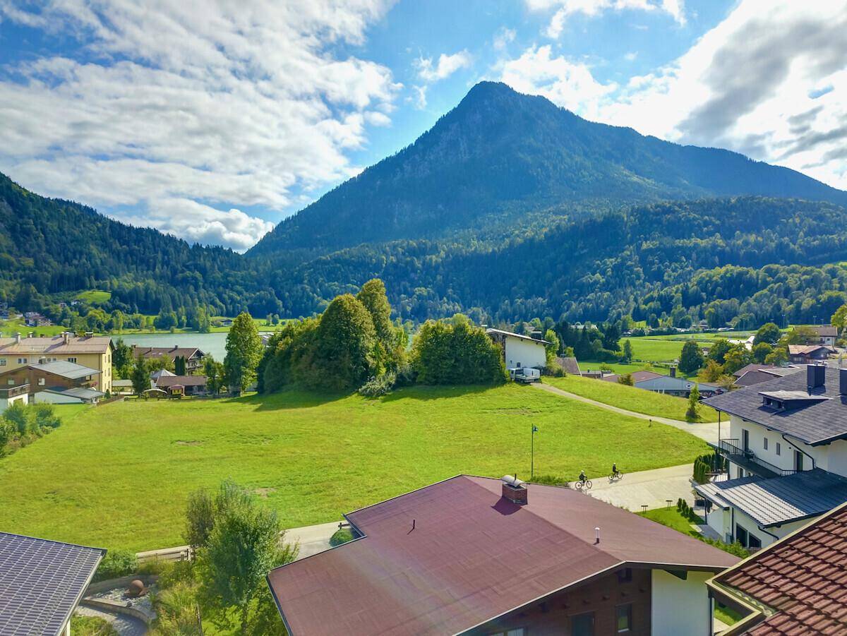 Panoramablick auf eine malerische Seenlandschaft umgeben von majestätischen Bergen und grünen Wiesen.
