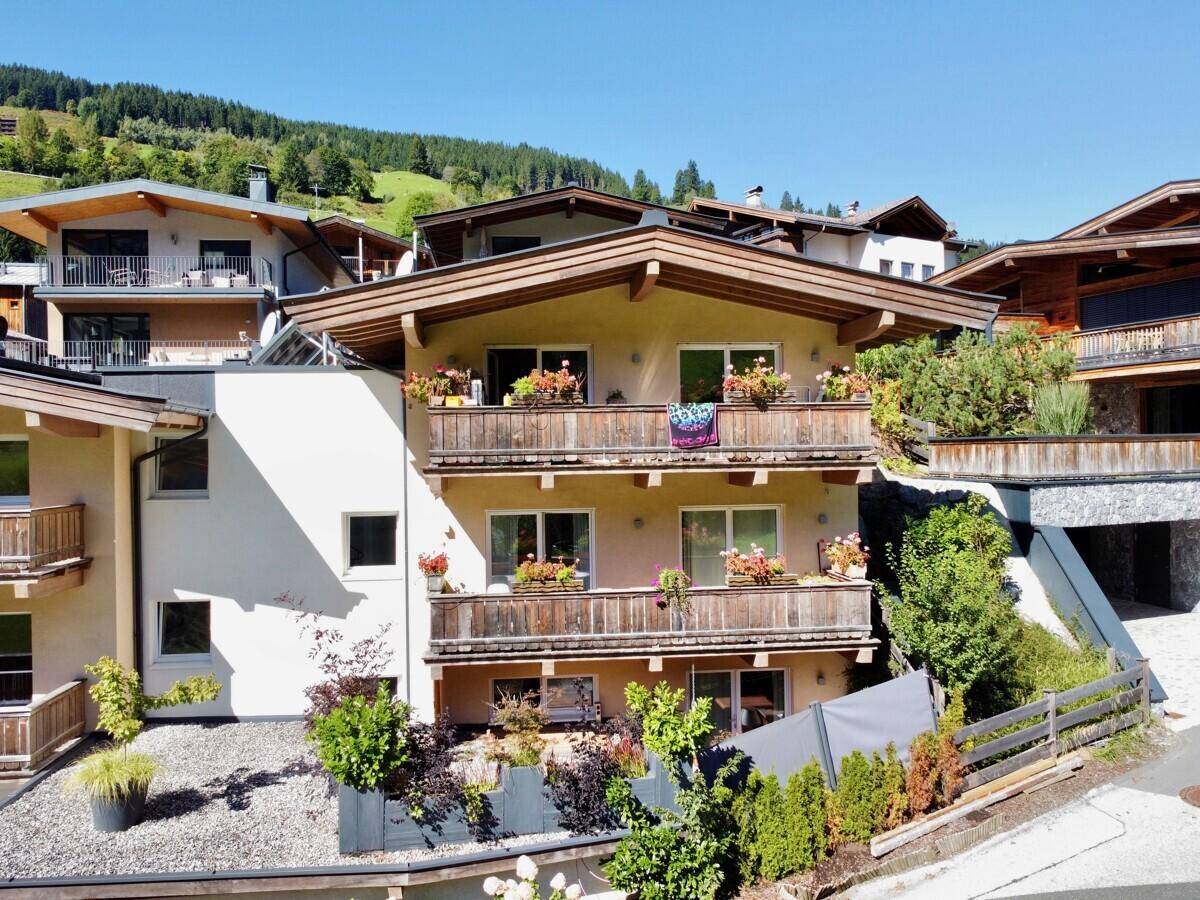 Mehrstöckiges Wohnhaus im alpinen Stil mit Balkonen und Blumenkästen an einem Hang.