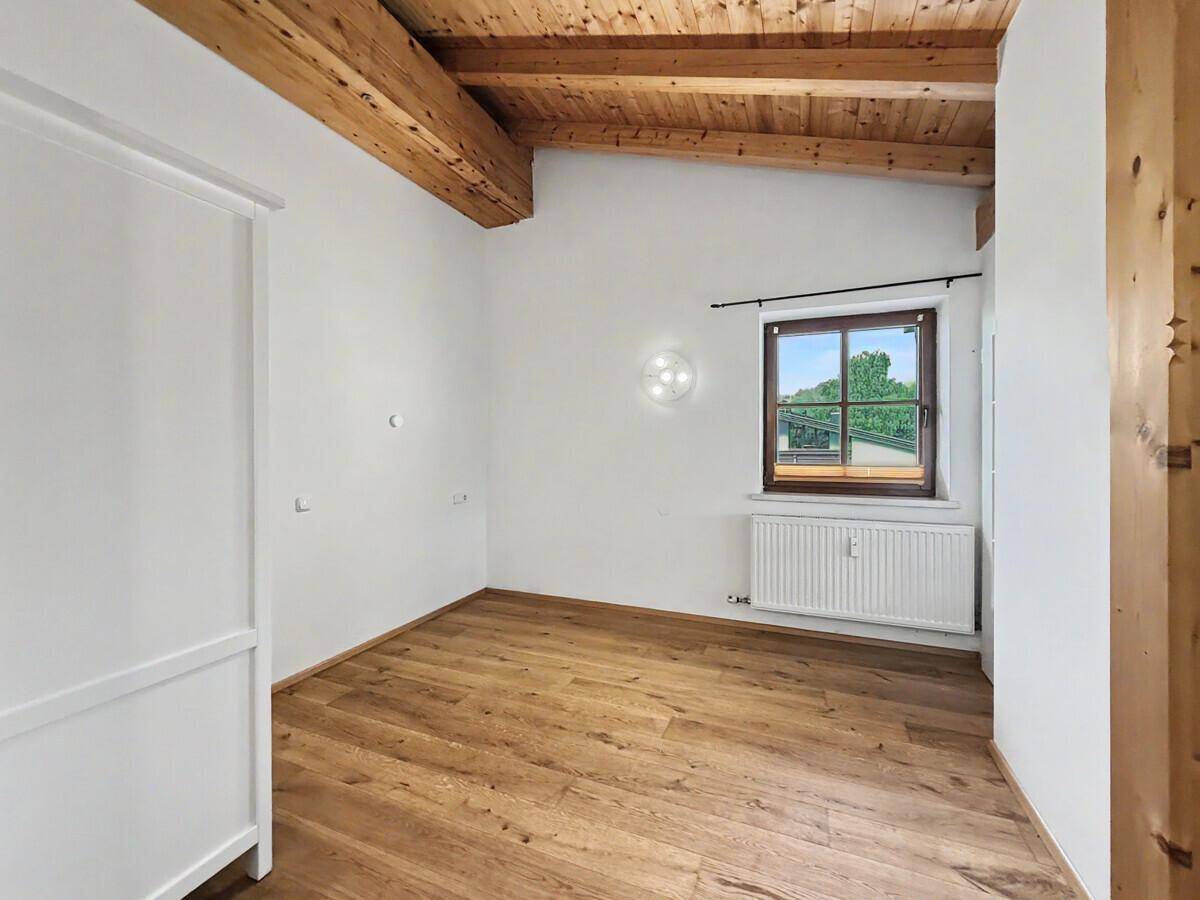 Helles Schlafzimmer mit Holzbalkendecke, Holzboden und Fenster mit grüner Aussicht.
