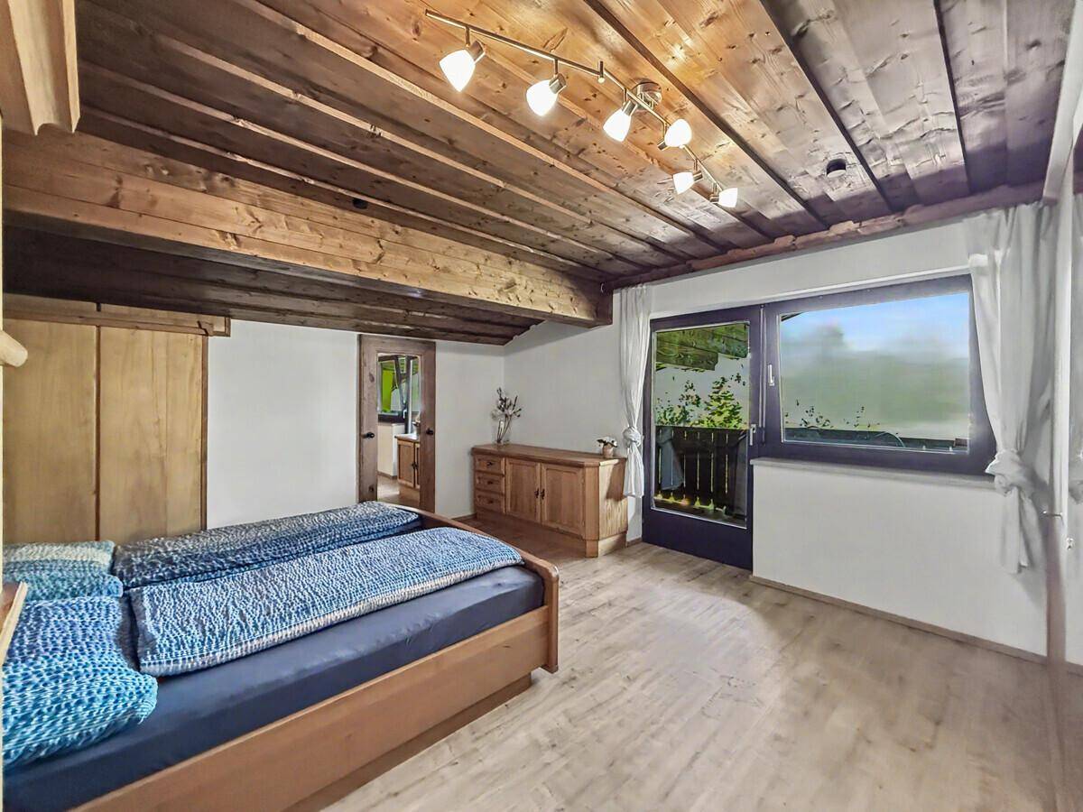 Schlafzimmer mit Holzbalkendecke und Zugang zu einem Balkon, bietet eine gemütliche Atmosphäre.