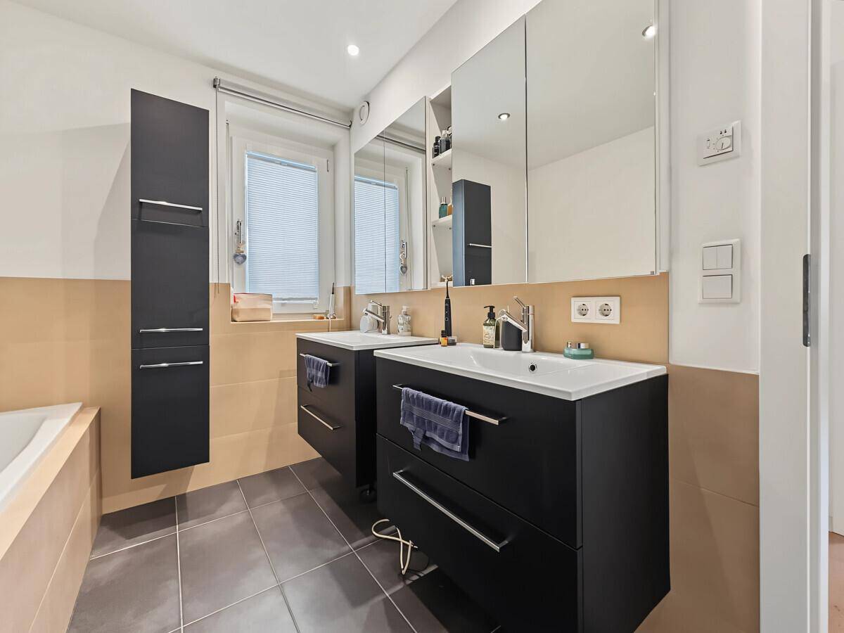 Helles Badezimmer mit Doppelwaschbecken, Spiegelschrank und Fenster für Tageslicht.