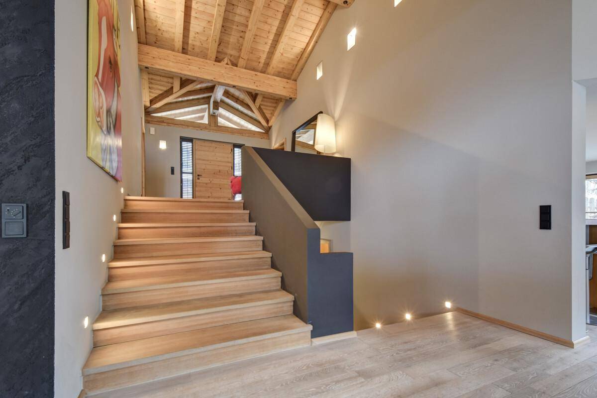 Moderner Treppenaufgang aus Holz mit indirekter Beleuchtung und hohen Decken.
