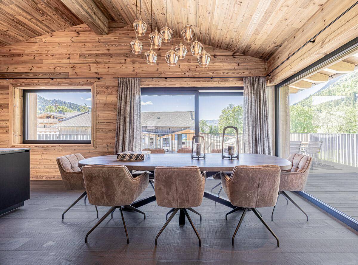 Eleganter Essbereich mit großem Holztisch, bequemen Stühlen und Zugang zur Terrasse mit Bergblick.