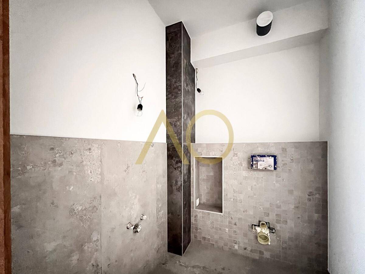 Unfertiges Badezimmer mit modernen Fliesen an den Wänden und vorbereiteten Anschlüssen.