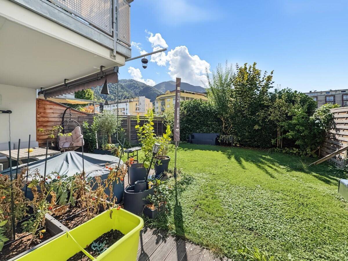Sonniger Garten mit Holzterrasse, Hochbeeten und Blick auf die umliegende Berglandschaft.