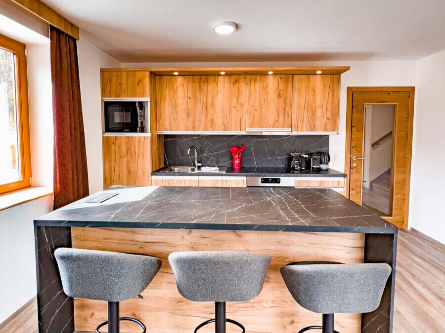 Helle Küche mit Holzfronten, dunkler Kücheninsel und Barhockern für Essbereich.