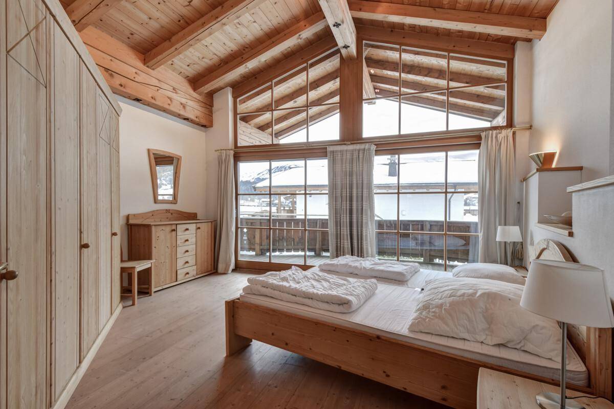 Großzügiges Schlafzimmer mit hohen Decken, Holzbalken und großen Fenstern mit Bergblick.