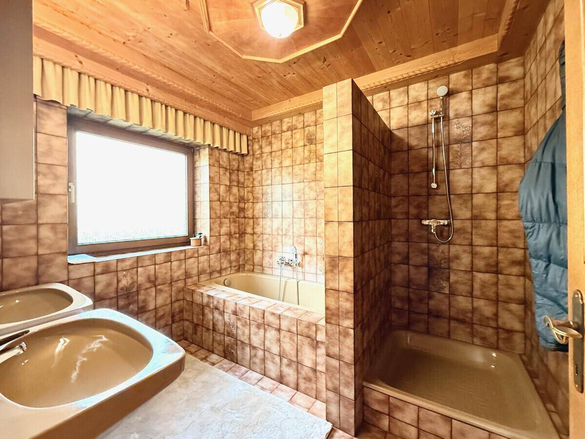 Badezimmer im 80er-Jahre-Stil mit braunen Fliesen, Badewanne und Dusche.