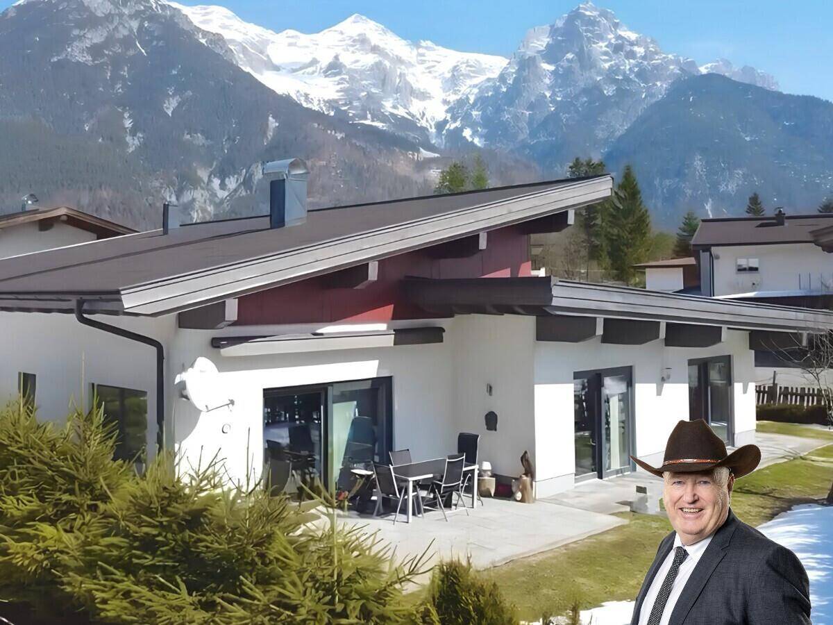 Modernes Haus mit großer Terrasse und Sitzbereich, umgeben von einer beeindruckenden Berglandschaft.