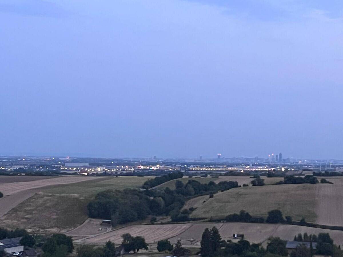 Panoramablick über eine ländliche Landschaft in der Dämmerung mit einer entfernten Stadtkulisse am Horizont.