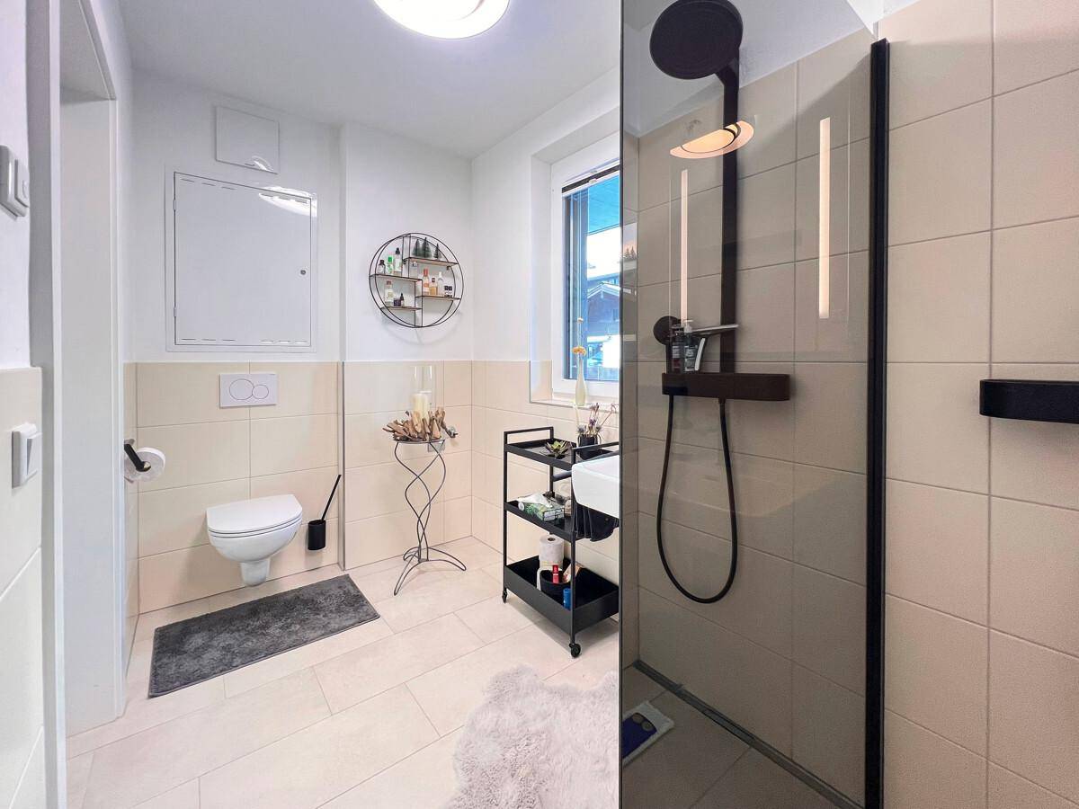 Modernes Badezimmer mit begehbarer Dusche, Wand-WC und hellen Fliesen.