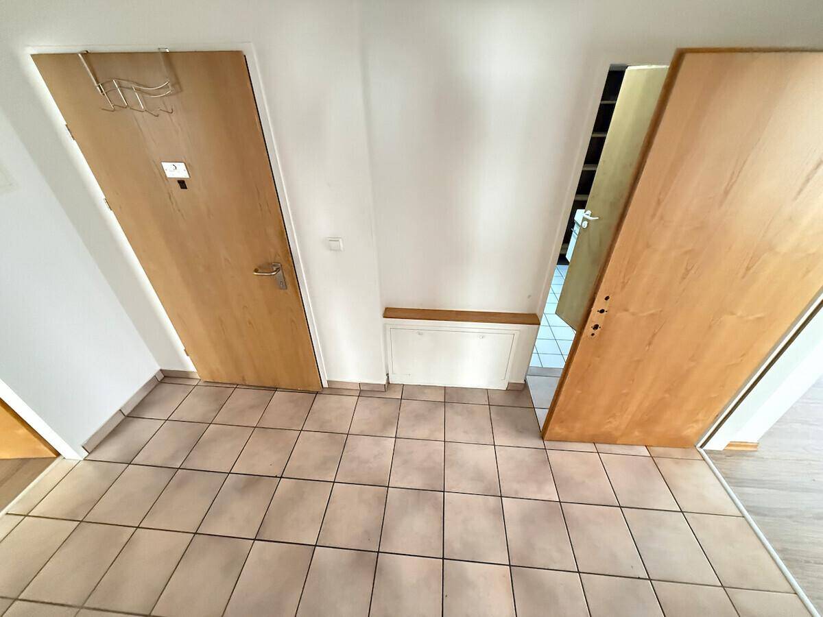 Eingangsbereich mit Fliesenboden, weißen Wänden und Holztüren.