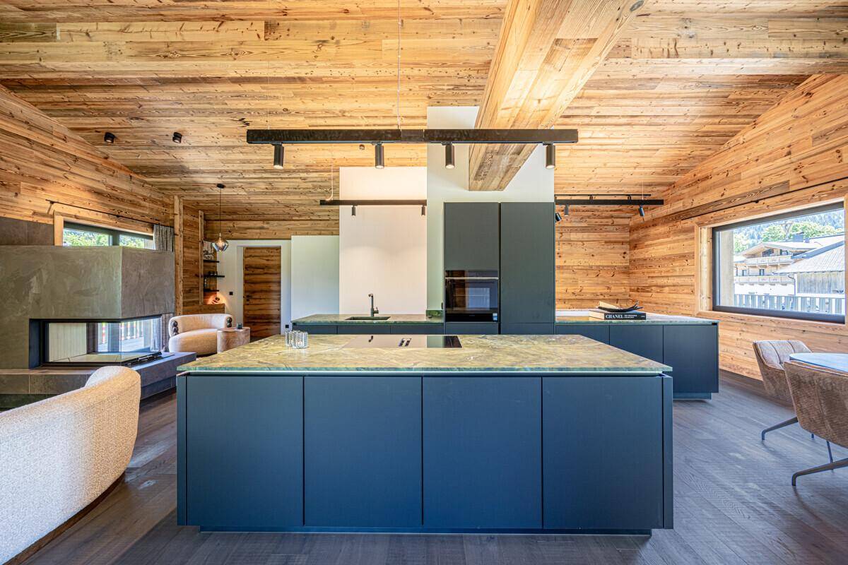 Moderne offene Küche mit dunklen Schränken, Kücheninsel und integrierten Geräten im alpinen Wohnbereich.