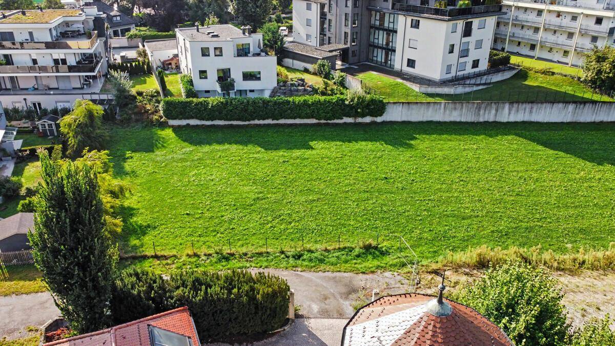 Luftaufnahme einer weitläufigen Grünfläche, umgeben von Wohngebäuden und einer Mauer.