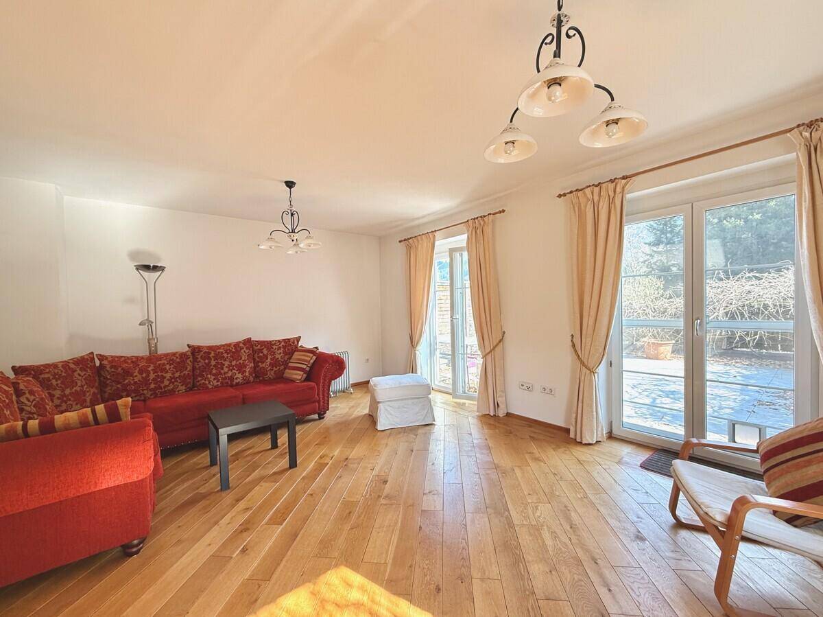 Gemütliches Wohnzimmer mit rotem Sofa, Holzboden und großzügigem Zugang zur Terrasse.