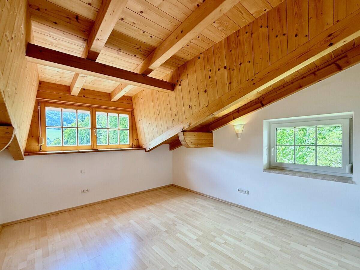 Geräumiges Schlafzimmer im Dachgeschoss mit Holzbalkendecke und Fenstern mit Bergblick.
