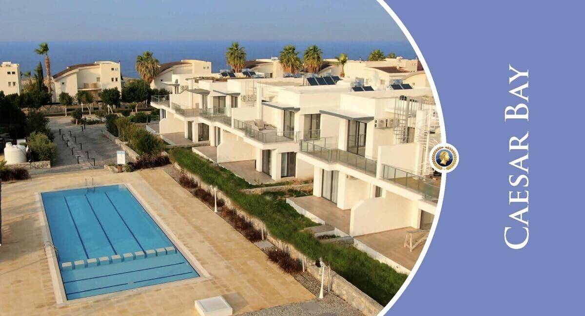 Luftaufnahme des Caesar Bay Resorts mit modernen weißen Gebäuden, Pools und grünen Hecken am Meer.