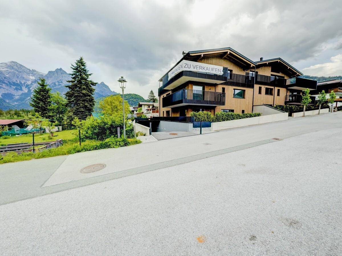 Modernes Gebäude mit Holzfassade und Balkonen in alpiner Umgebung mit Bergblick.