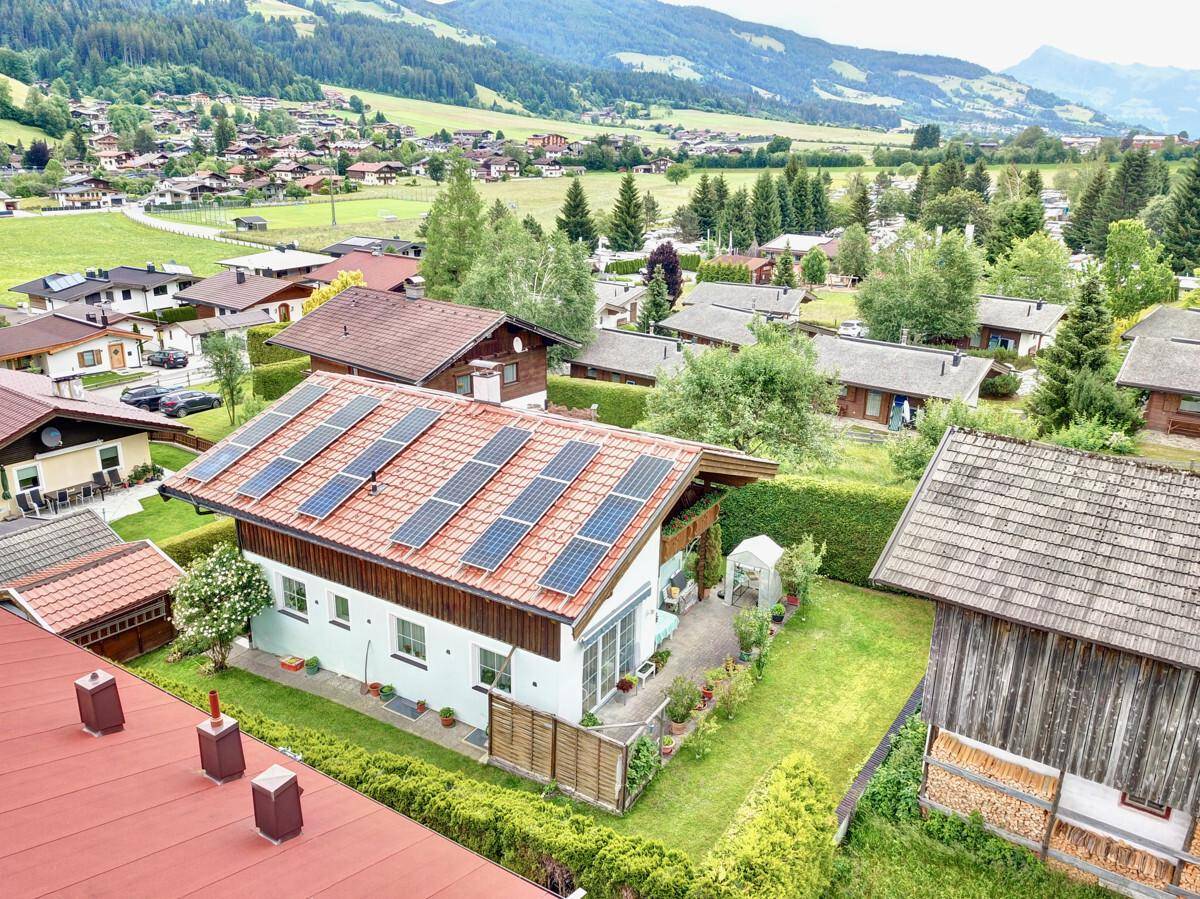 Panoramablick auf ein Haus mit Solaranlage und die umliegende ländliche Siedlung mit Bergen im Hintergrund.
