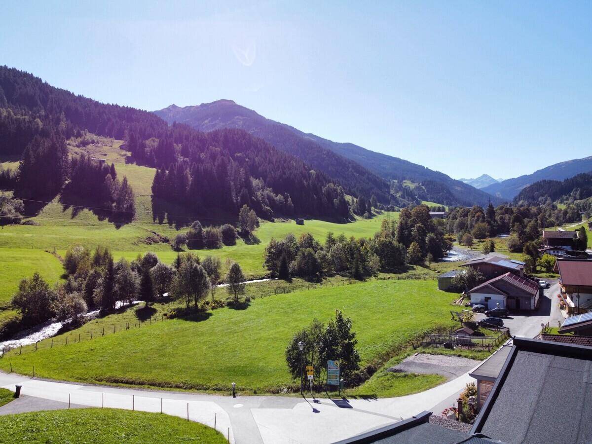 Weitläufiger Blick auf die grüne Berglandschaft mit Häusern und einem Bachlauf.