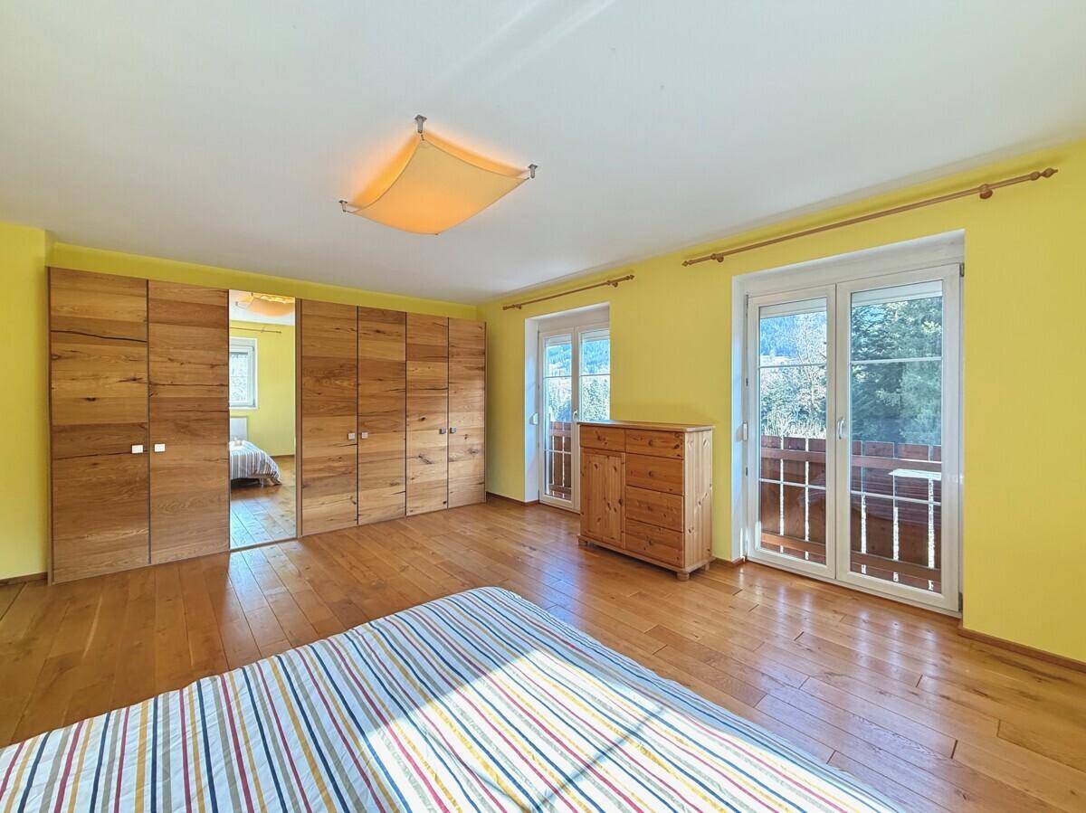 Helles Schlafzimmer mit Holzboden, gelben Wänden, Einbauschränken und Zugang zum Balkon.