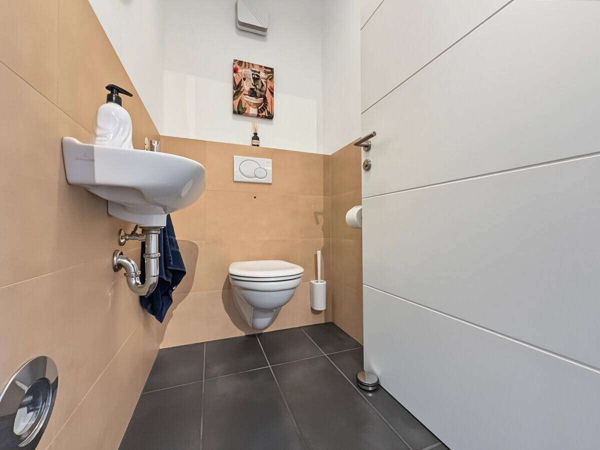 Modernes Gäste-WC mit Wand-WC, Waschbecken und beigefarbenen Fliesen.