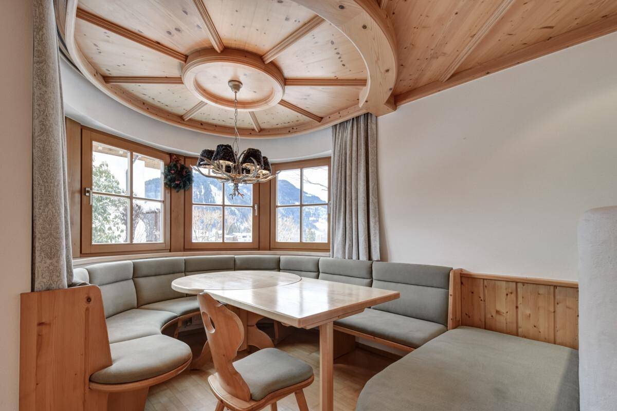 Traditioneller Essbereich mit Holztisch und Eckbank, umgeben von Fenstern mit Bergblick.