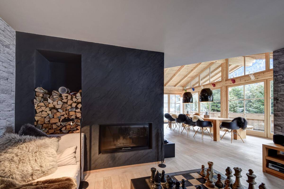 Offener Wohnbereich mit modernem Kamin, Holzstapel und Blick in den Essbereich.