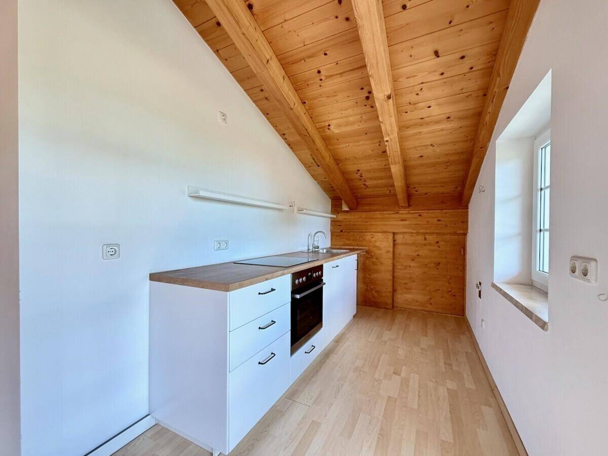 Kleine, moderne Küchenzeile mit Kochfeld und Backofen unter einer Holzbalkendecke.