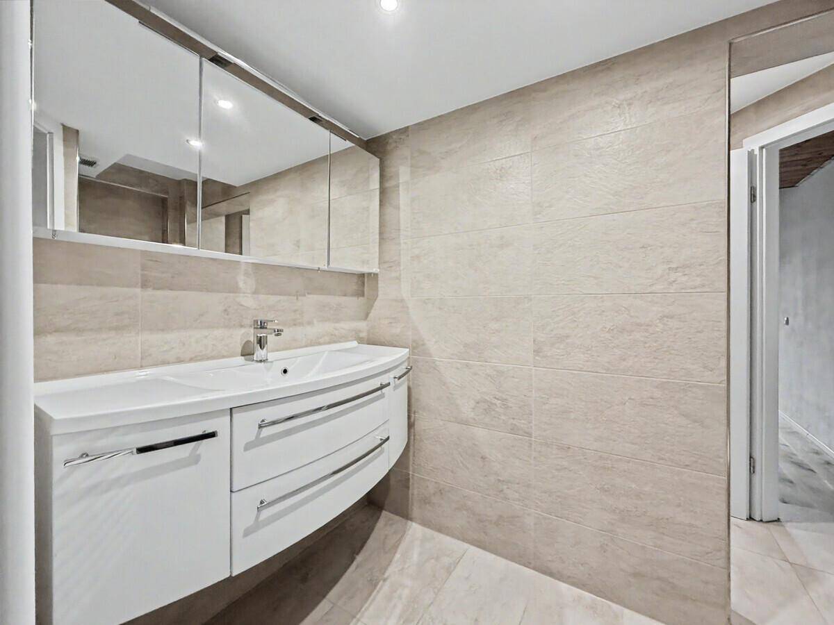 Elegantes Badezimmer mit modernem Waschtisch, Spiegelschrank und großformatigen Fliesen.