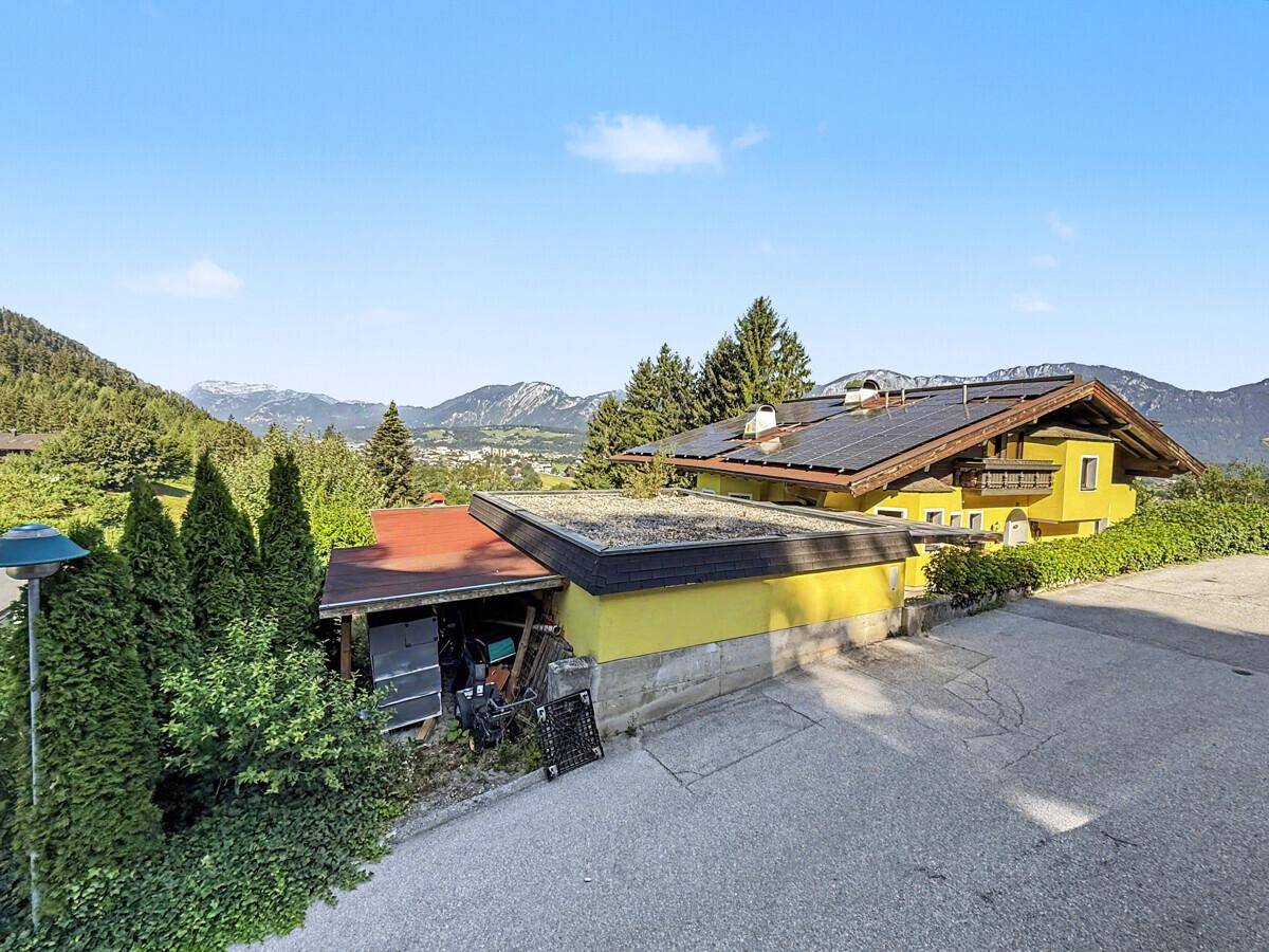 Ansicht des Hauses mit gelber Fassade und Solaranlage, eingebettet in die grüne Landschaft.
