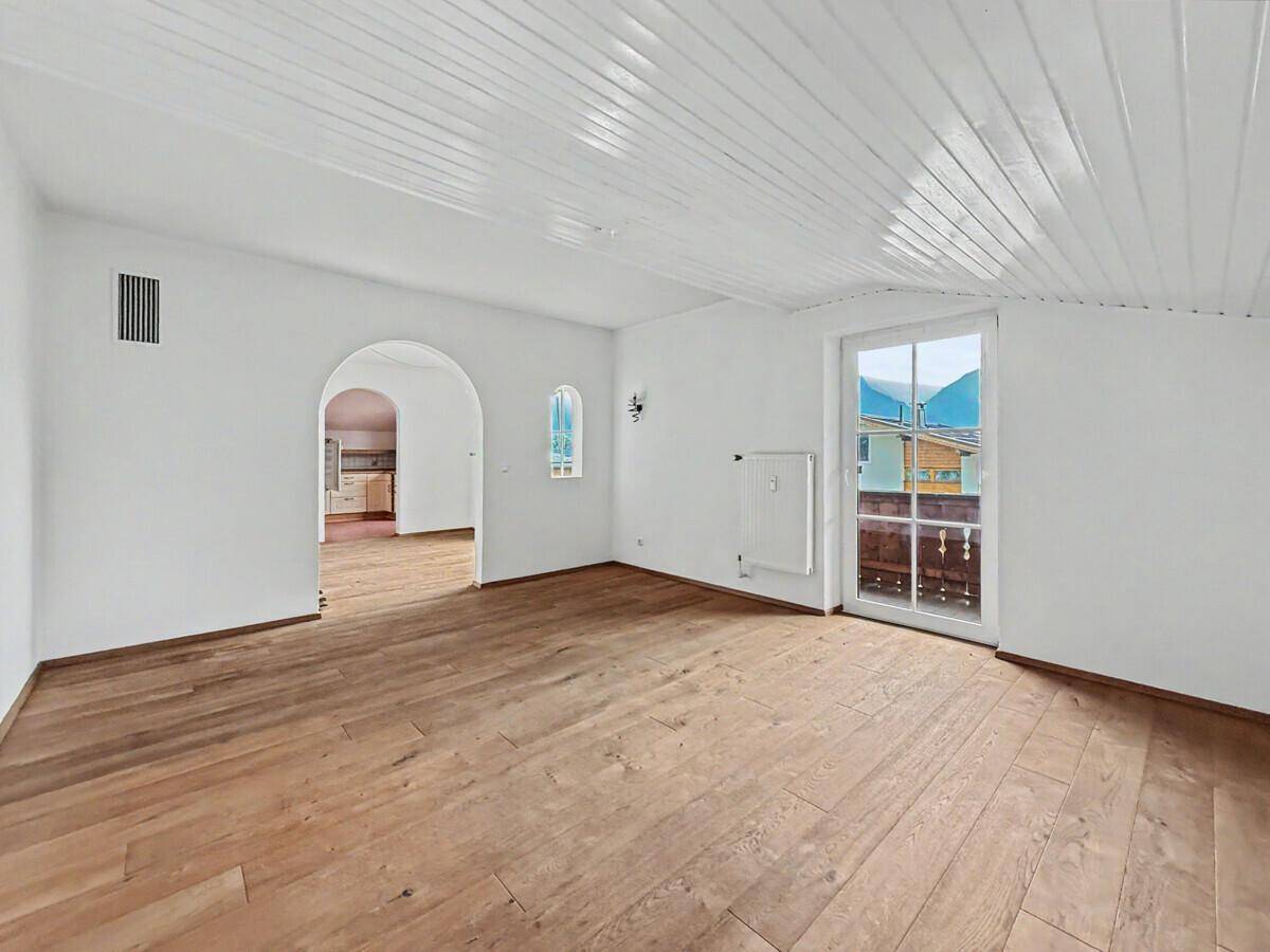 Helles Wohnzimmer mit Holzboden, weißer Holzdecke und Balkonzugang mit Bergblick.