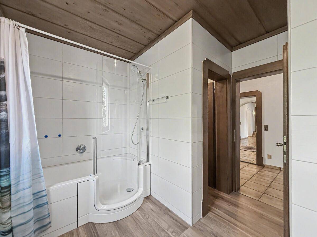 Modernes Badezimmer mit weißen Fliesen, Dusch-Badewannen-Kombination und Holzbalkendecke.