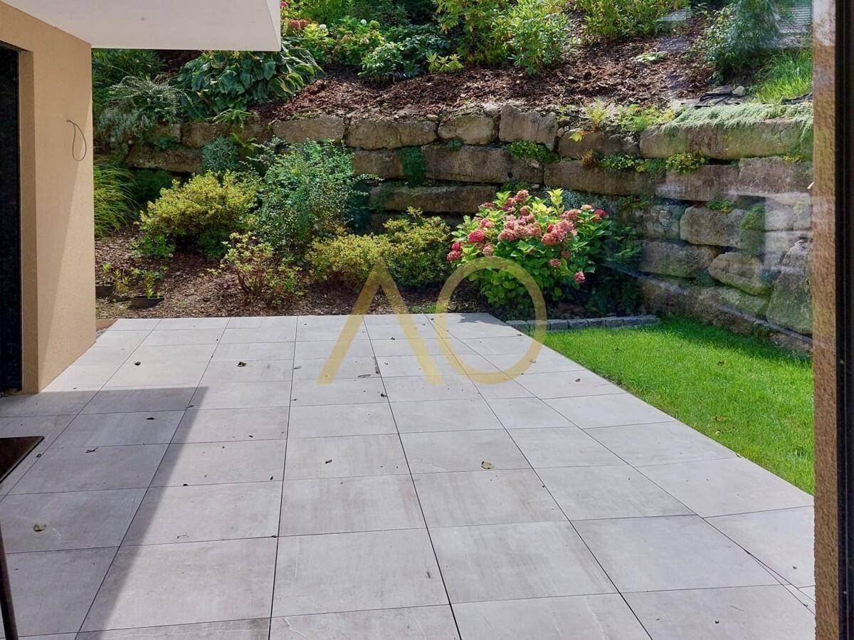 Blick auf die gepflasterte Terrasse und den grünen Garten mit blühenden Sträuchern.