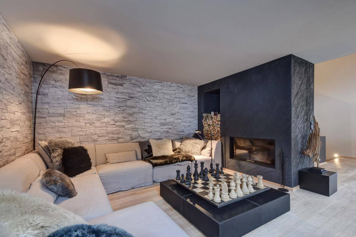 Gemütliches Wohnzimmer mit Kamin, Steinwand und Schachbrett auf dem Couchtisch.