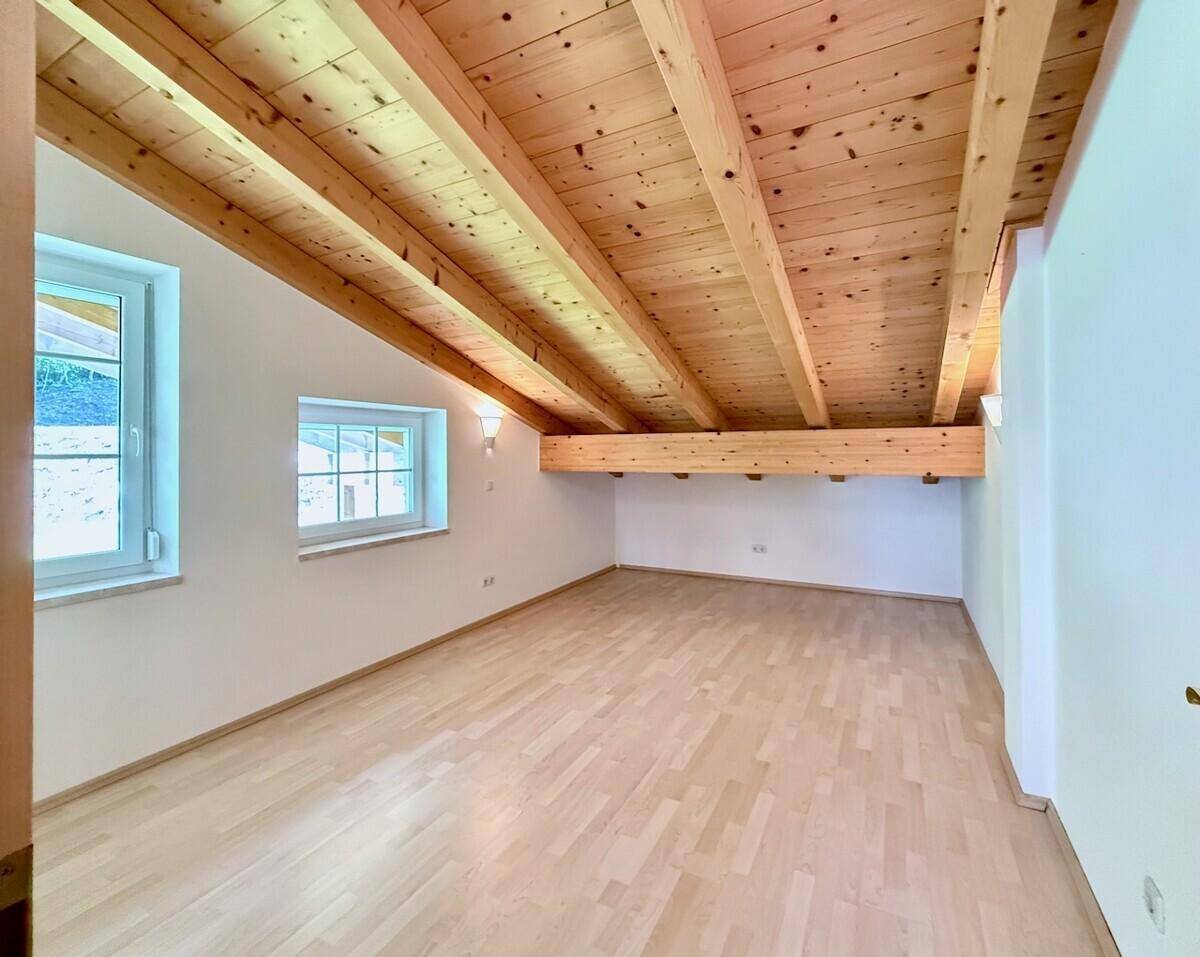 Geräumiges Schlafzimmer mit Holzbalkendecke, Parkettboden und zwei Fenstern.