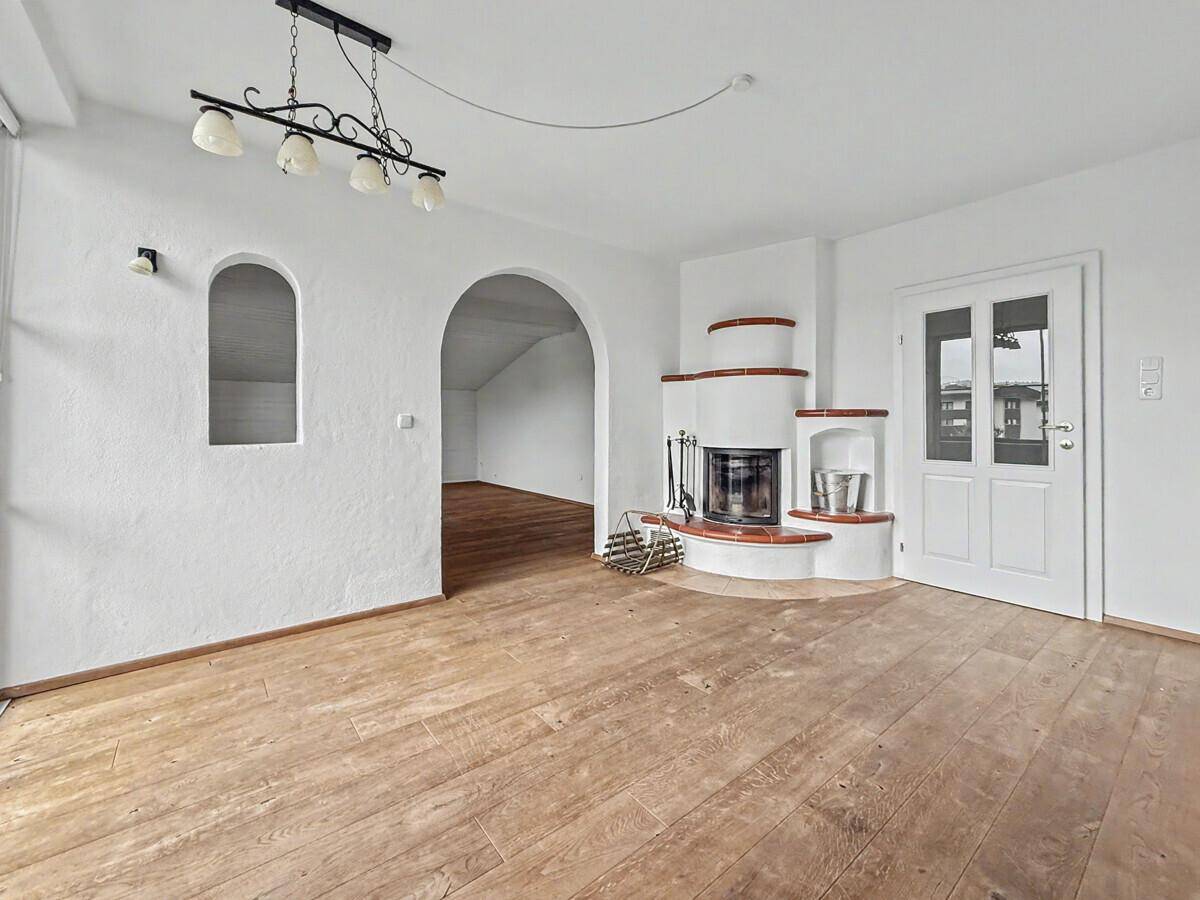 Helles Wohnzimmer mit traditionellem Kamin, Holzboden und Zugang zu einem weiteren Raum.
