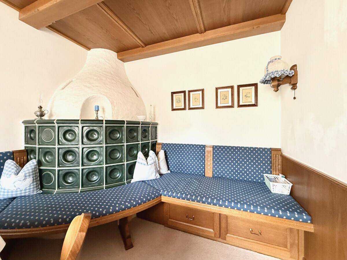 Gemütliche Sitzecke mit Kachelofen und traditionellen blauen Polstern im alpenländischen Stil.