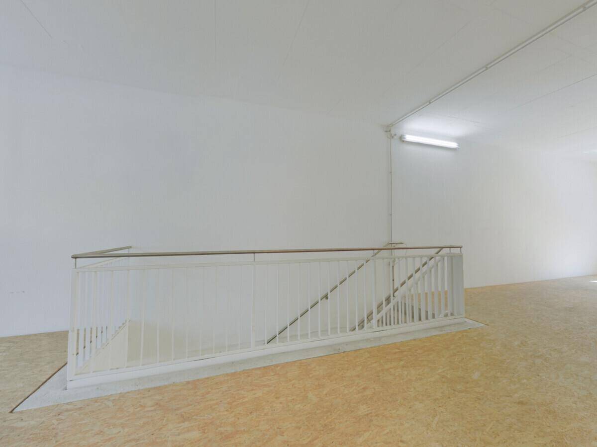 Weiß gestrichene Treppe mit Geländer in einem leeren Gewerberaum mit OSB-Boden und weißen Wänden.
