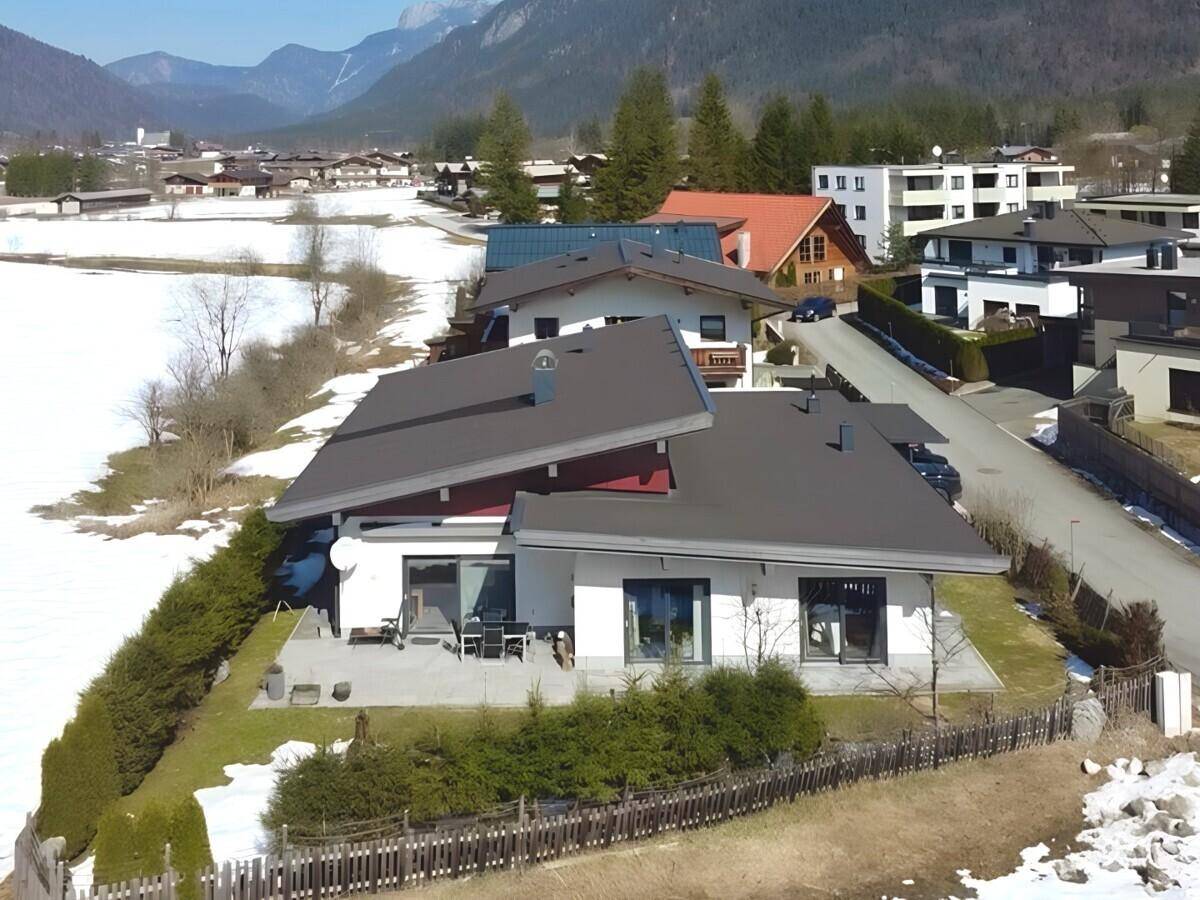 Luftaufnahme des modernen Hauses in alpiner Umgebung mit umliegenden Bergen und Schnee.