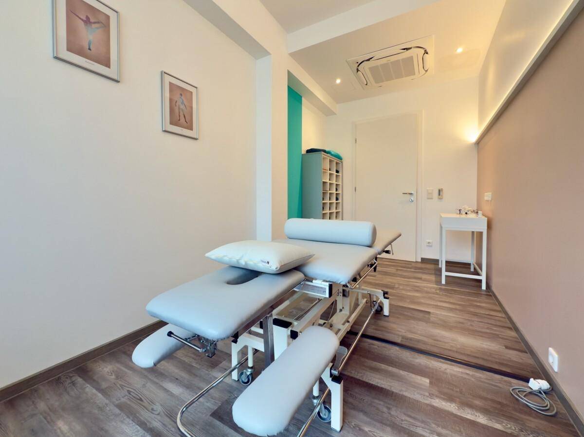 Heller Behandlungsraum mit verstellbarer Therapieliege und dezenter Wandgestaltung.