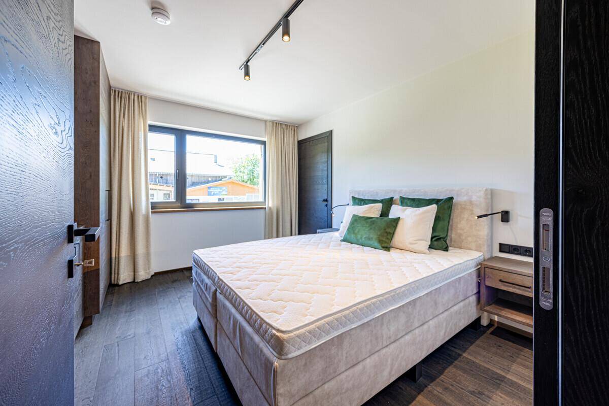 Helles Schlafzimmer mit großem Bett, Holzboden und einem Fenster mit Blick nach draußen.