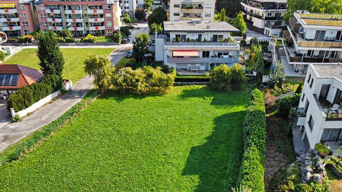 Luftaufnahme einer weitläufigen Grünfläche, umgeben von Wohngebäuden und einer Hecke.