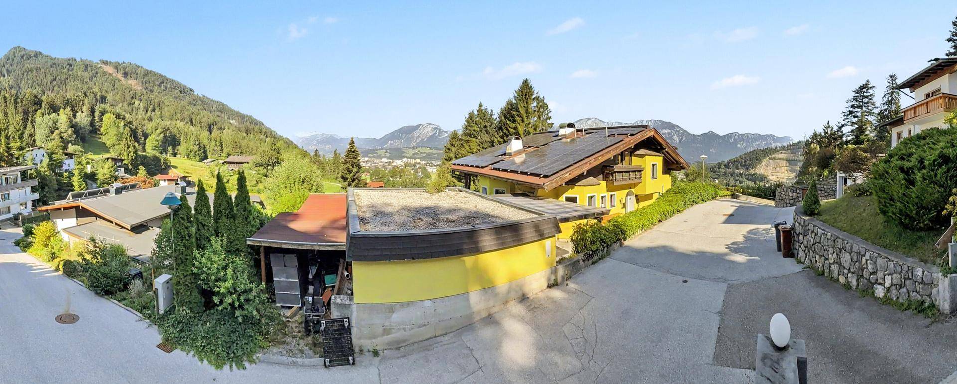 Panoramablick auf mehrere Häuser in einer bergigen Landschaft mit viel Grün und klarem Himmel.