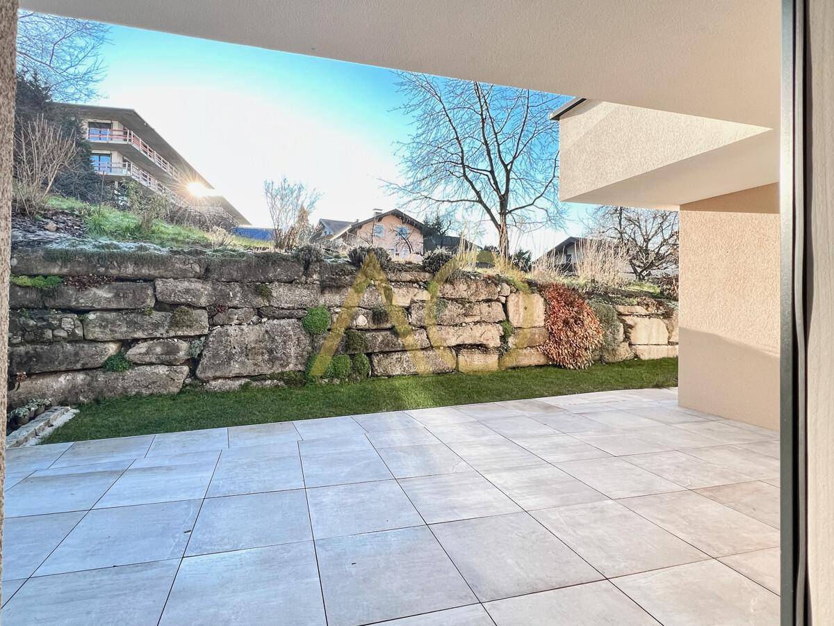 Geflieste Terrasse mit Blick auf eine begrünte Steinmauer und den Gartenbereich.
