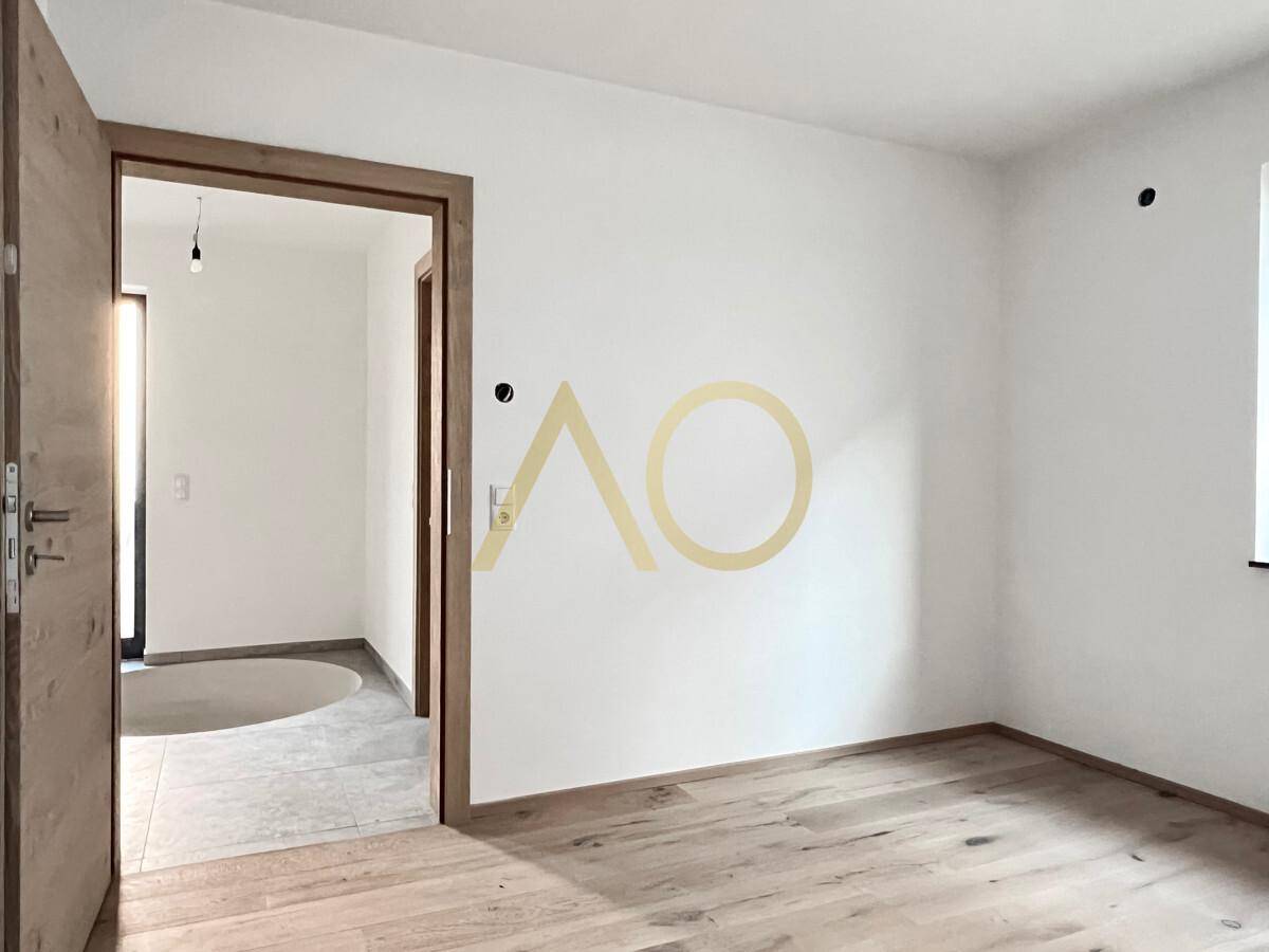 Schlafzimmer mit hellem Holzboden, weiß gestrichenen Wänden und Holztür.